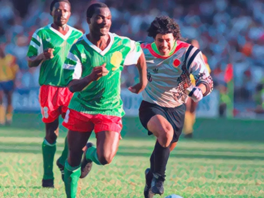 Il portiere colombiano René Higuita rincorre disperatamente l'attaccante del Camerun Roger Milla, che scappa verso la porta vuota dopo avergli rubato il pallone sulla trequarti