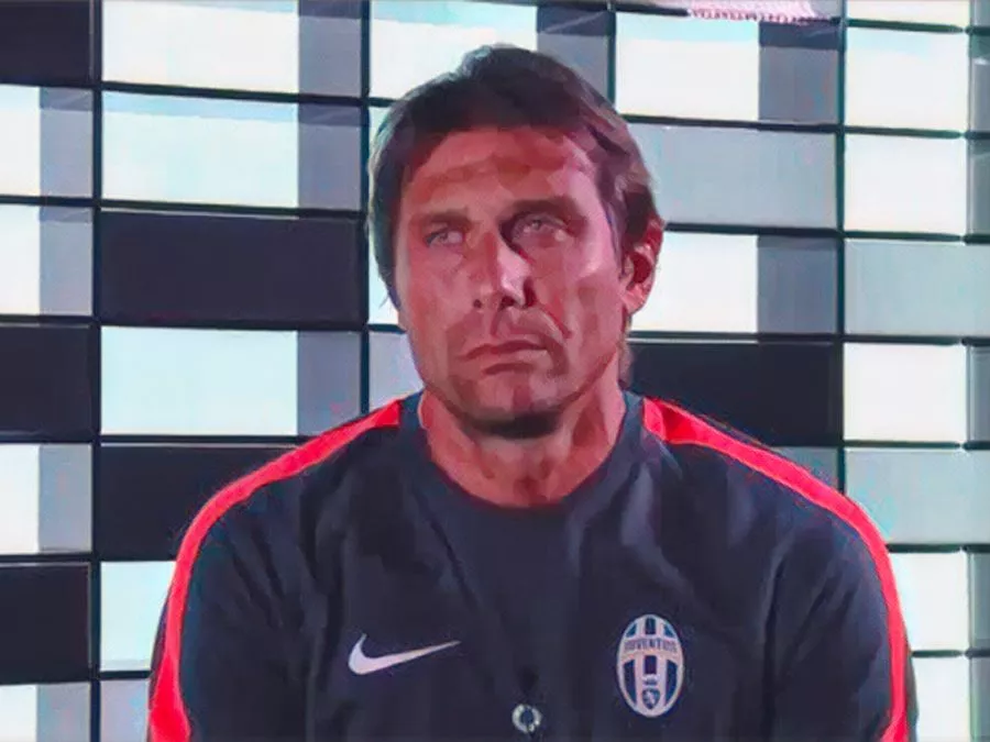 Primo piano di Antonio Conte con lo sguardo cupo e le braccia conserte durante la sua ultima intervista rilasciata ai canali ufficiali della Juventus il 15 luglio 2014