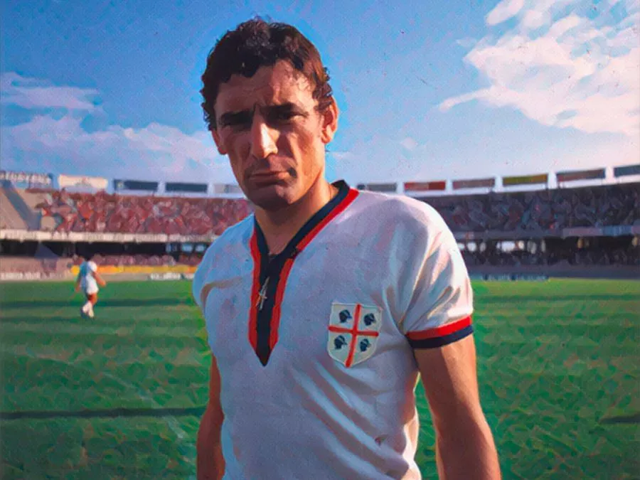 Gigi Riva in maglia rossoblù con lo scudetto del Cagliari sul petto fissa l'orizzonte fiero sotto il cielo della Sardegna negli anni '70
