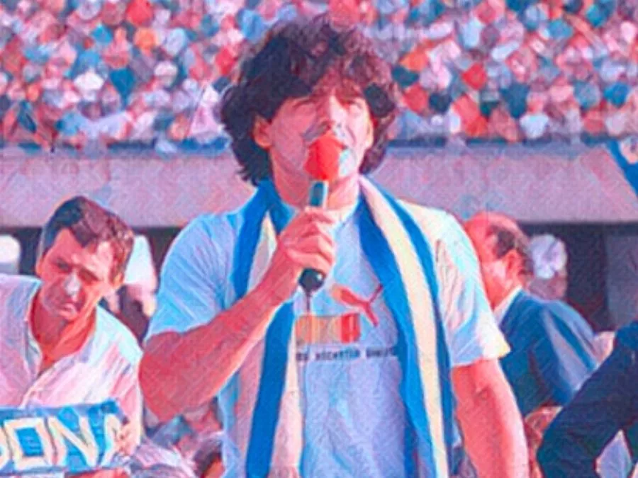 Diego Armando Maradona sorridente con i capelli ricci e la maglietta azzurra mentre saluta i 60 mila tifosi del Napoli stipati sulle tribune dello Stadio San Paolo il 5 luglio 1984